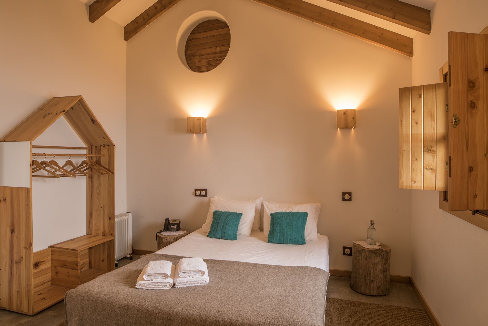 A bedroom with a bed, two wall-mounted lights, a wooden headboard, a mirror, and a wooden wardrobe.
