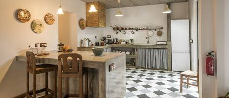 Een keuken met een geruit vloertje, houten stoelen, een bargedeelte, hangende lampen en diverse keukengerei.