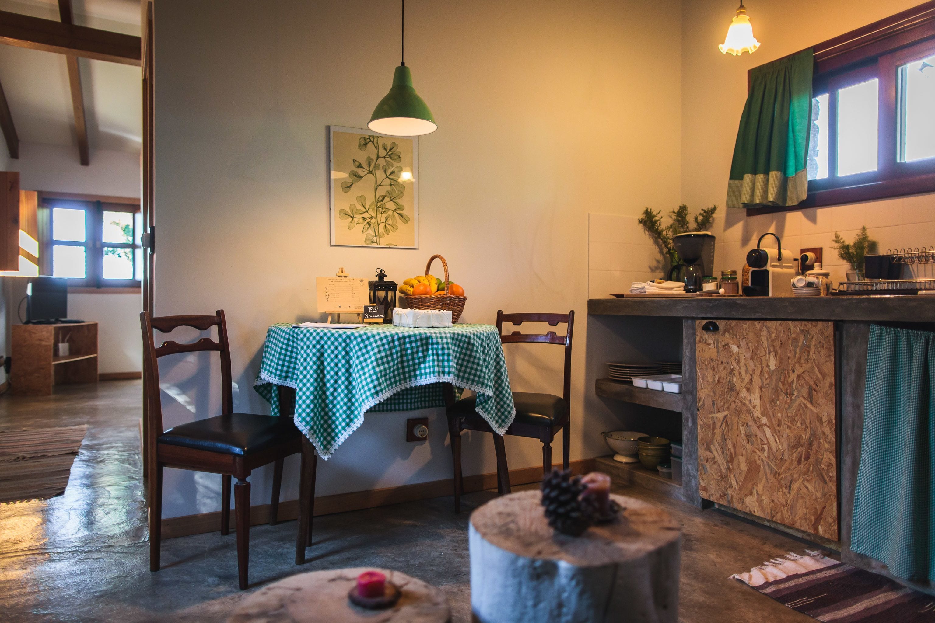 A cozy kitchen with a wooden table, chairs, a hanging light, and a window with curtains.