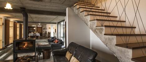 A modern living room with a fireplace, leather sofa, and a staircase with geometric wall design.
