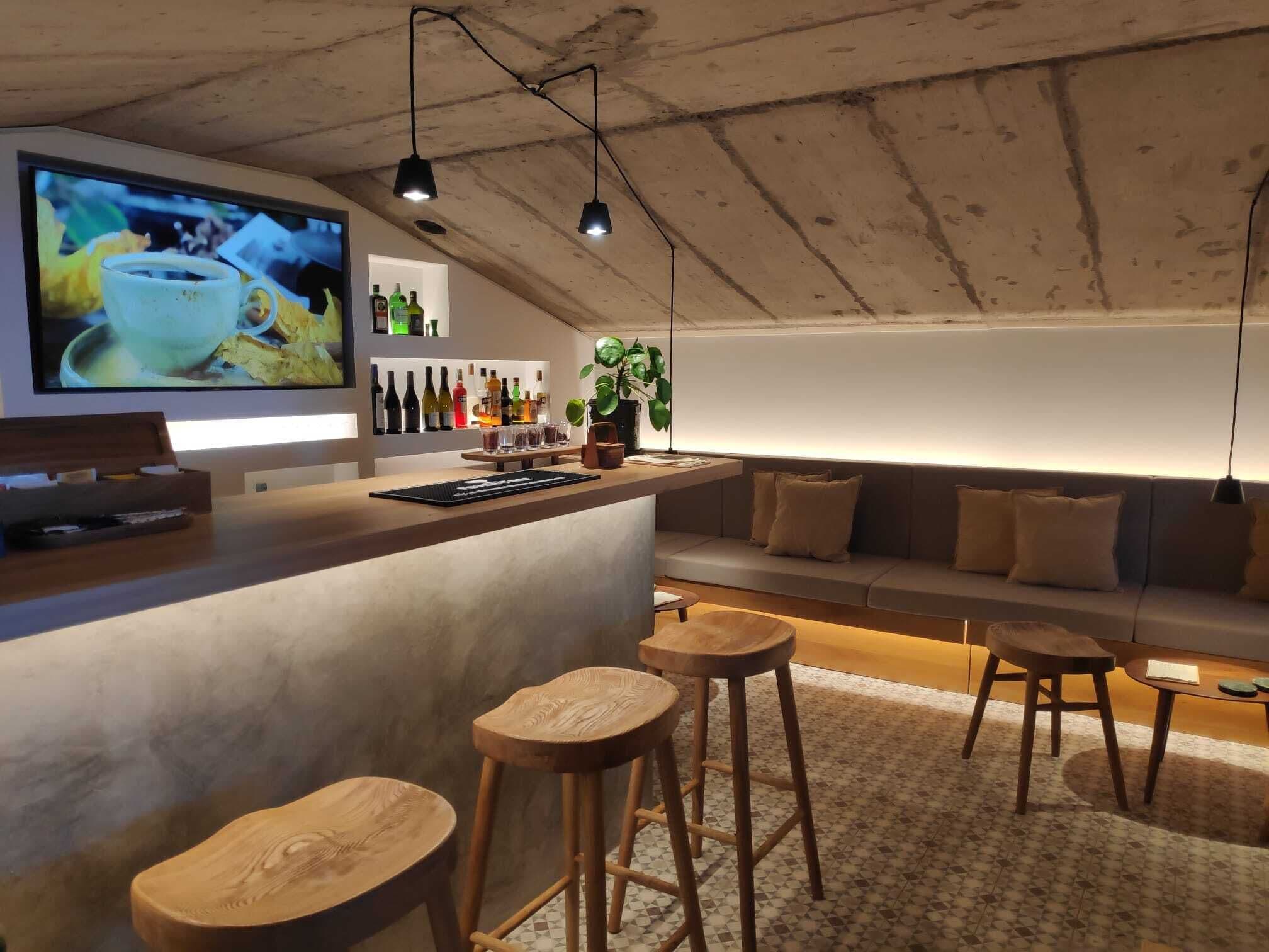 Un espace bar moderne avec un comptoir en bois, des tabourets et un coin salon agrémenté de coussins.