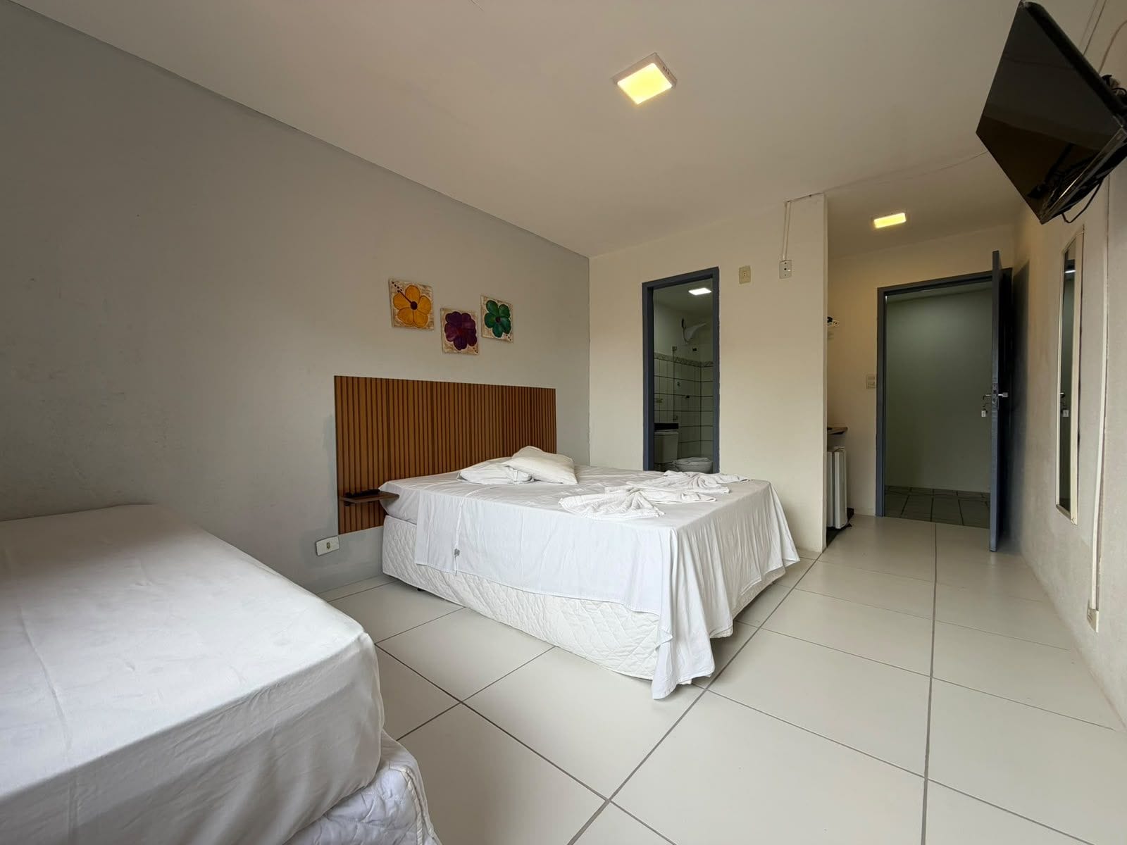 Camera d'albergo con due letti, una testiera in legno, una TV a schermo piatto e un bagno visibile attraverso una porta aperta.