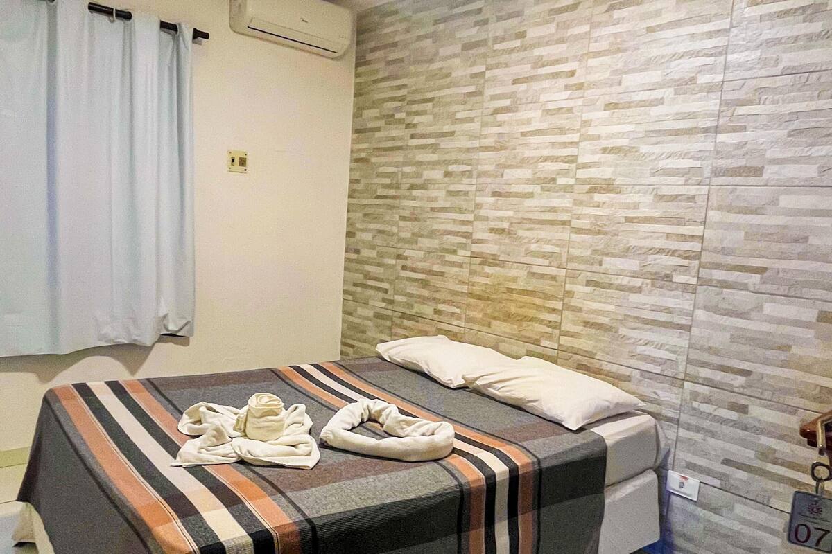 Quarto de hotel com cama, ar condicionado fixado na parede e chão de azulejos.