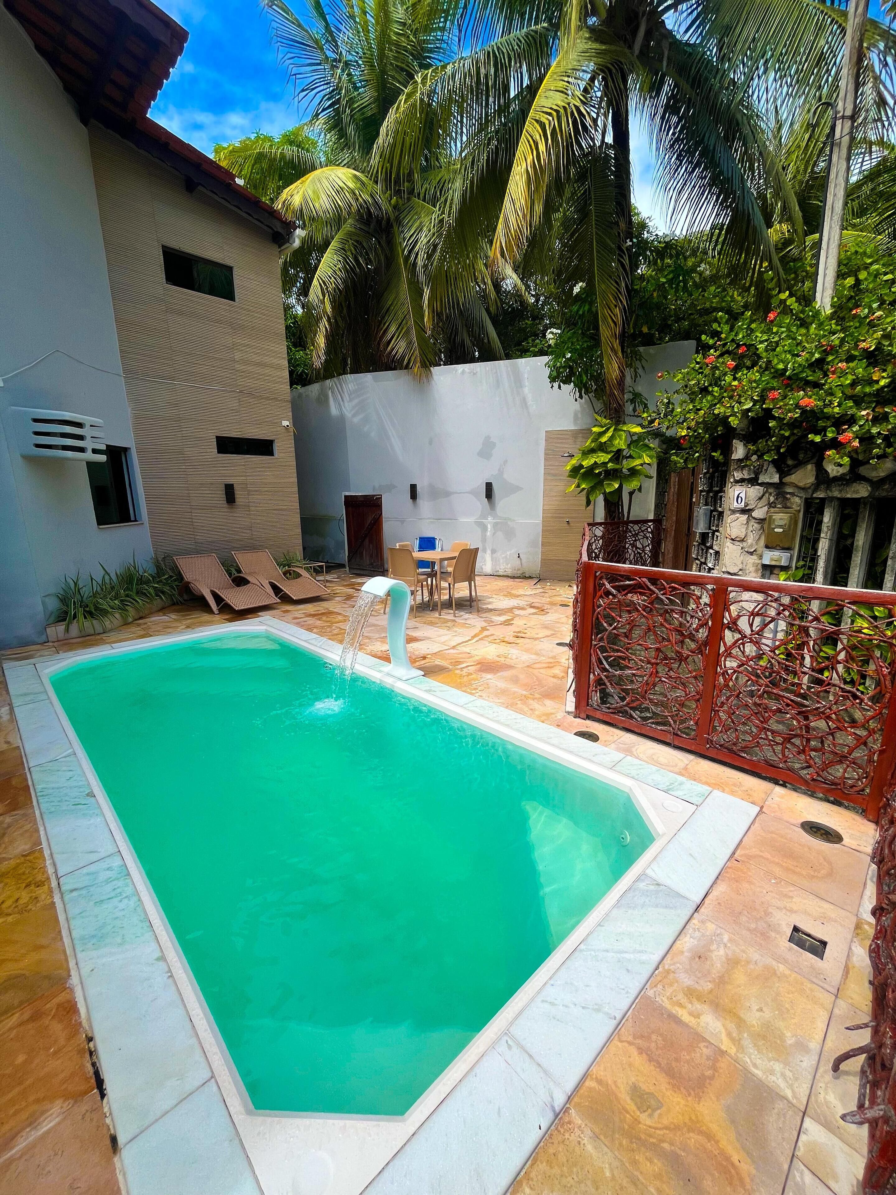 A rectangular swimming pool with a water feature, surrounded by a tiled patio.
