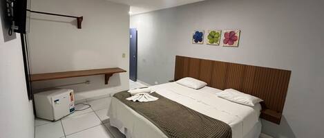A hotel room with a bed, a TV, a shelf, and a wall with flower paintings.