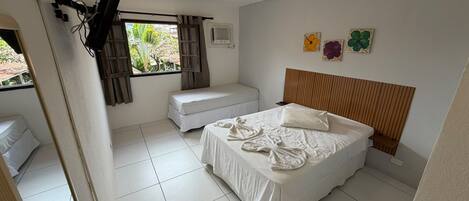 A bedroom with a bed, a bench, a window with curtains, and a wall with floral artwork.