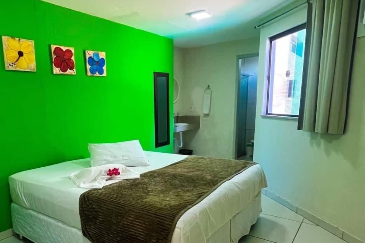 Quarto com parede verde, cama com roupa de cama branca e janela com cortinas.