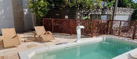 Ein Schwimmbecken mit gefliestem Sonnendeck, umgeben von Palmen und einer Steinmauer.