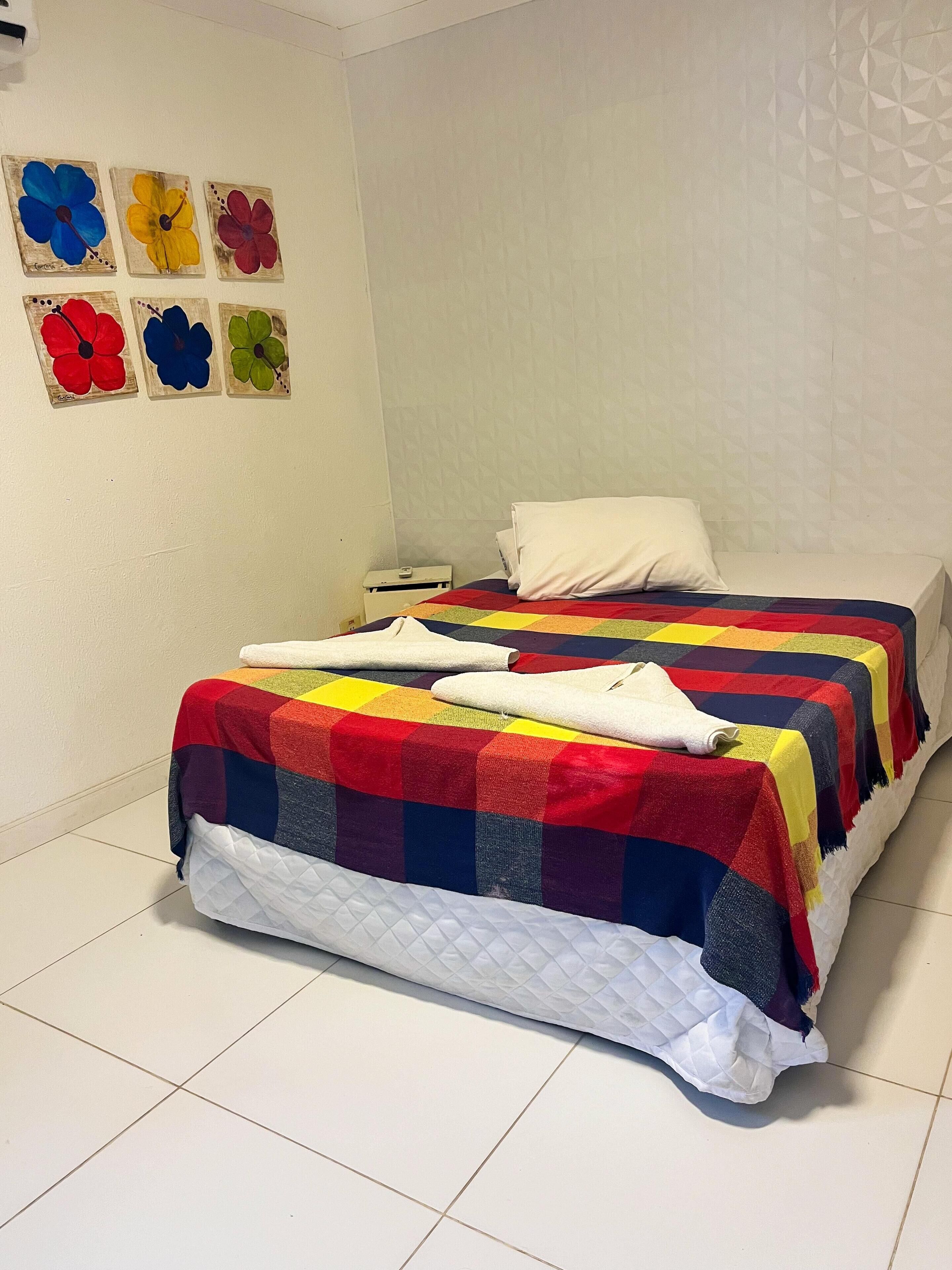 A bed with a colorful quilt, a white pillow, and a quilted white duvet.