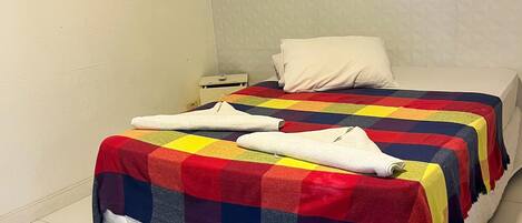 A bed with a colorful quilt, a white pillow, and a quilted white duvet.
