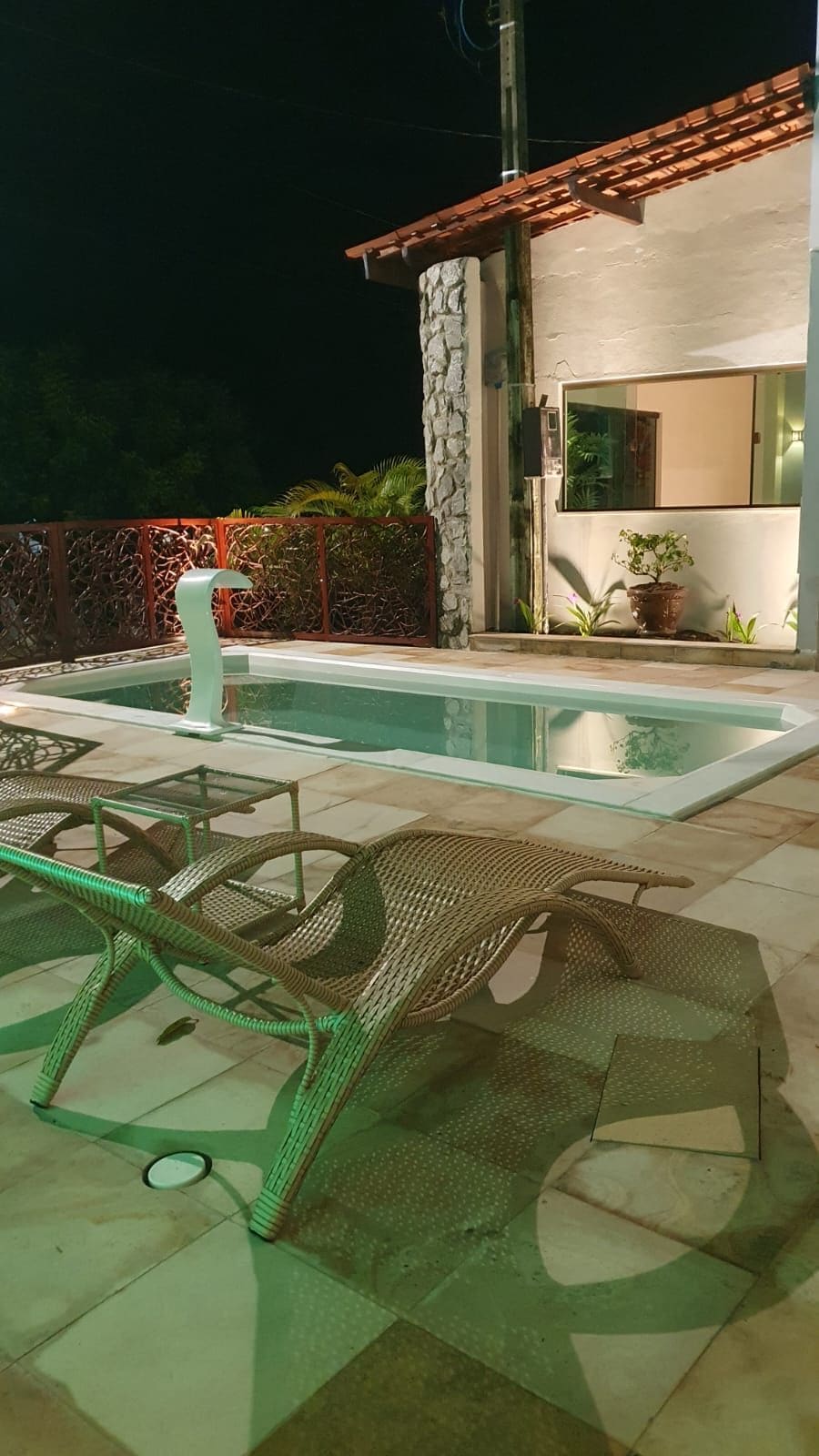 A swimming pool with lounge chairs, a stone wall, and a modern building with a tiled roof.