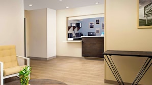 A reception area with a reception desk, a chair, a small table with a plant, and a wall-mounted sign. - WoodSpring Suites Fargo North Near NDSU (Fargo)