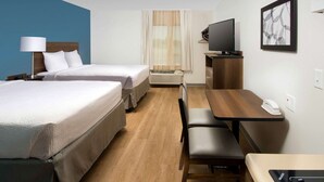 A hotel room with two beds, a desk, a chair, a television, and a window with curtains. - WoodSpring Suites Fargo North Near NDSU (Fargo)