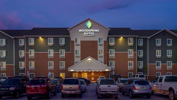 A hotel with a prominent sign reading "Woodspring Suites" and a number "1090" above the entrance. There are multiple cars parked in front. - WoodSpring Suites Fargo North Near NDSU (Fargo)