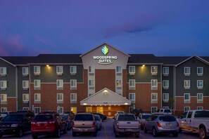 A hotel with a prominent sign reading "Woodspring Suites" and a number "1090" above the entrance. There are multiple cars parked in front.