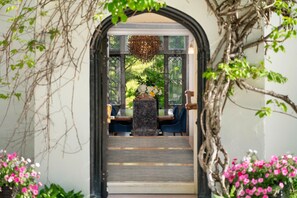 An indoor dining area with a central table and chairs, surrounded by a decorative archway and greenery.