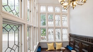 A room with a large bay window, a wooden bench with cushions, and a chandelier. - Seven Hills Inn (Lenox)