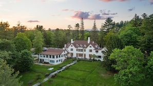 A large, white, multi-story house with a symmetrical design, surrounded by lush greenery and trees. - Seven Hills Inn (Lenox)