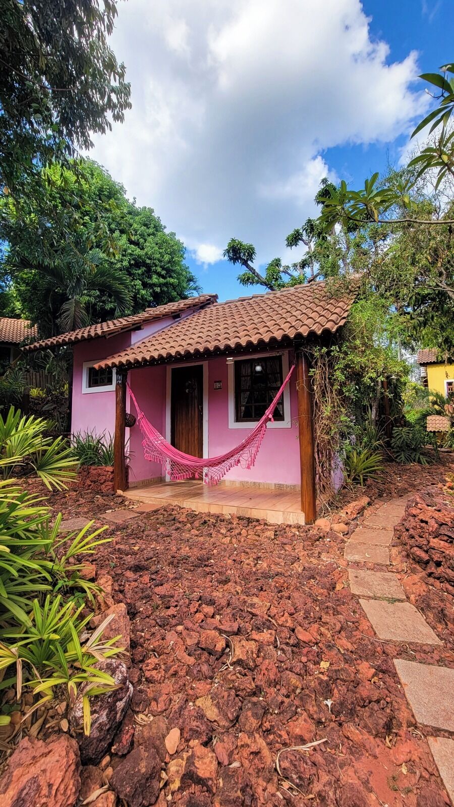 A small house with a tiled roof, a pink exterior, and a hammock in front.