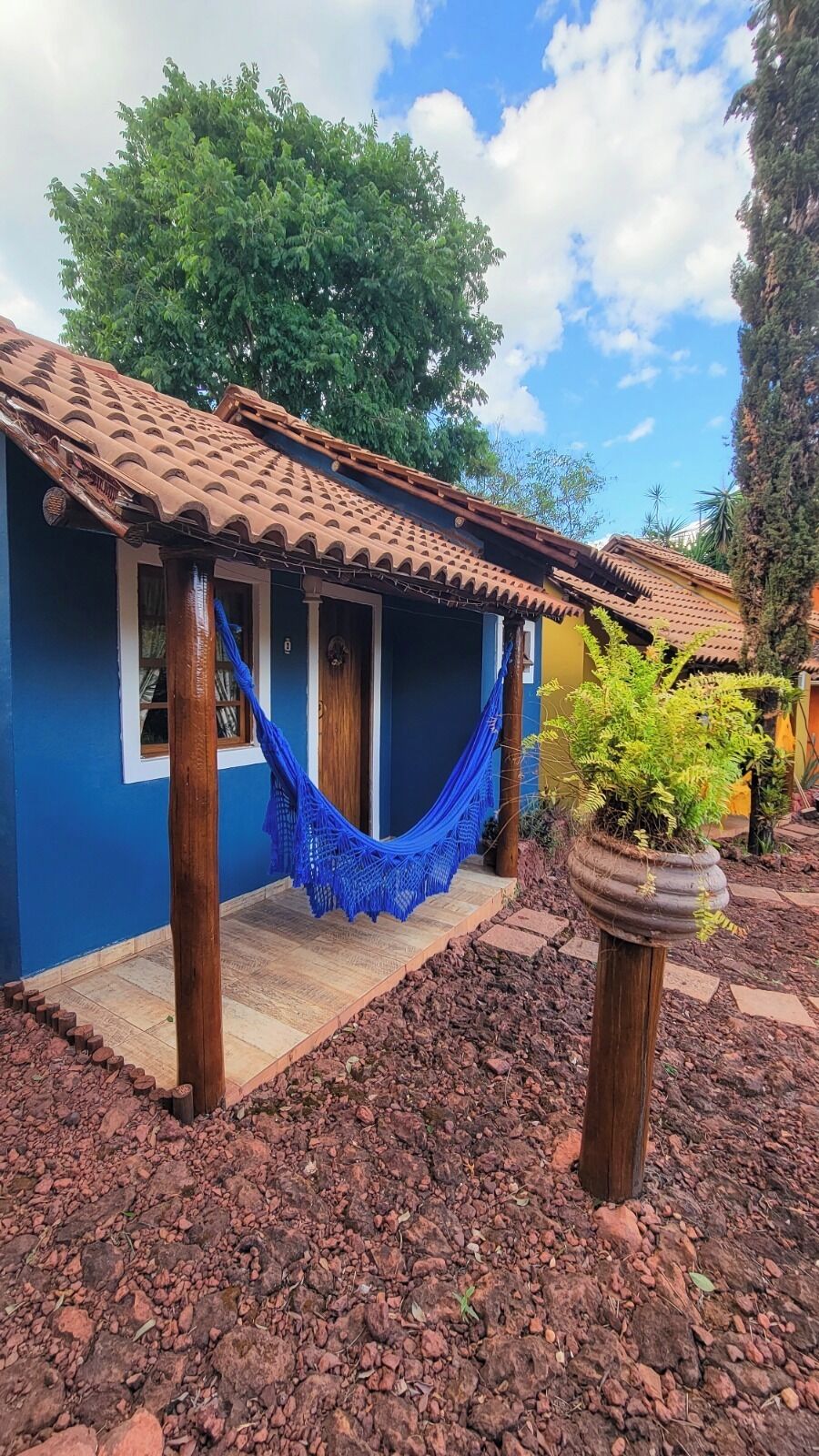 Una casa con techo de tejas, una hamaca y una planta en maceta.