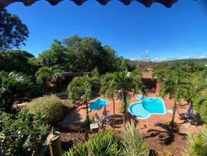 A pool area with two pools, surrounded by palm trees and a red-roofed building. - Pousada Mirante de Lençóis (Lençóis)
