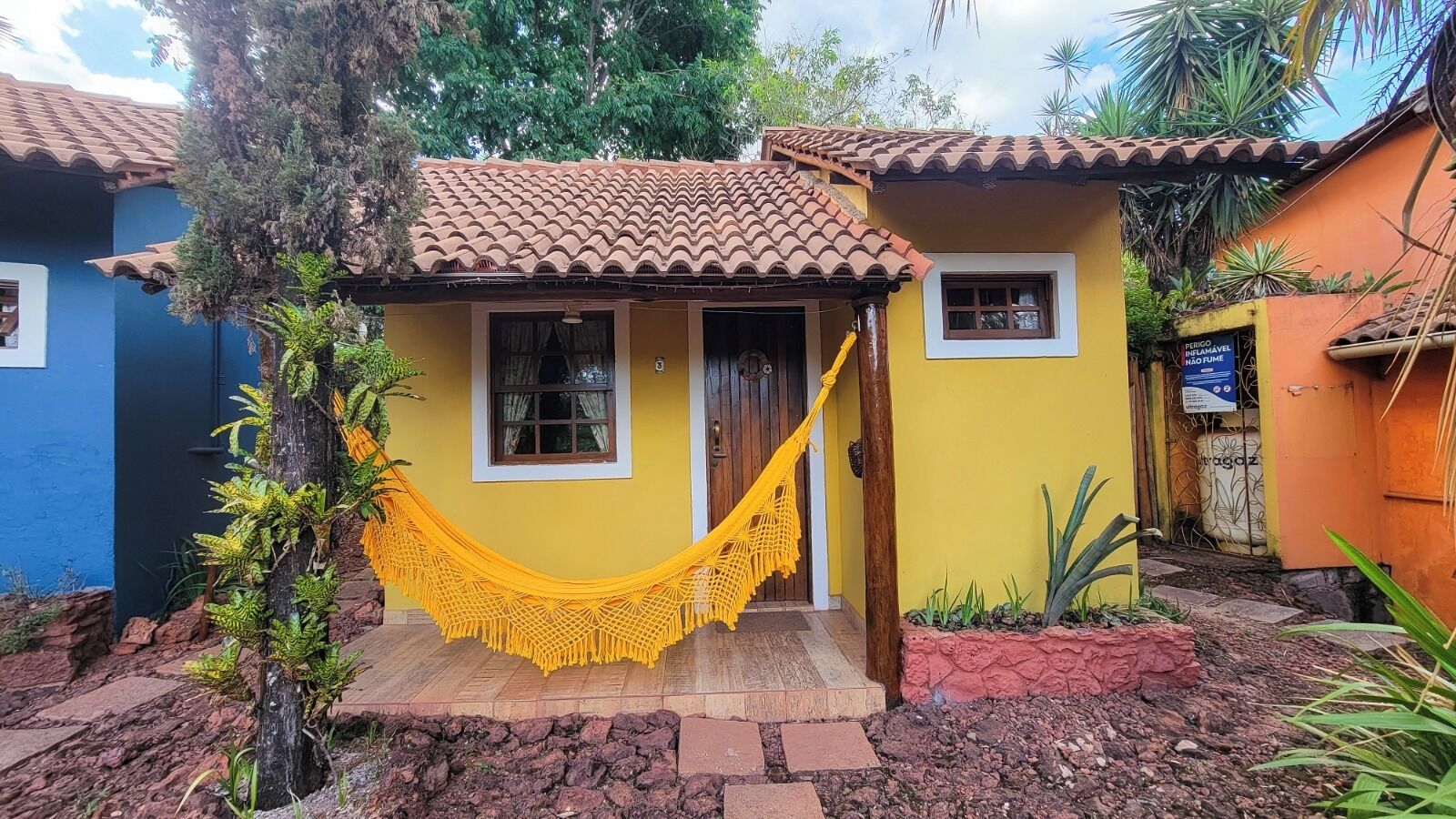 A yellow house with a tiled roof, a hammock, and a small porch.