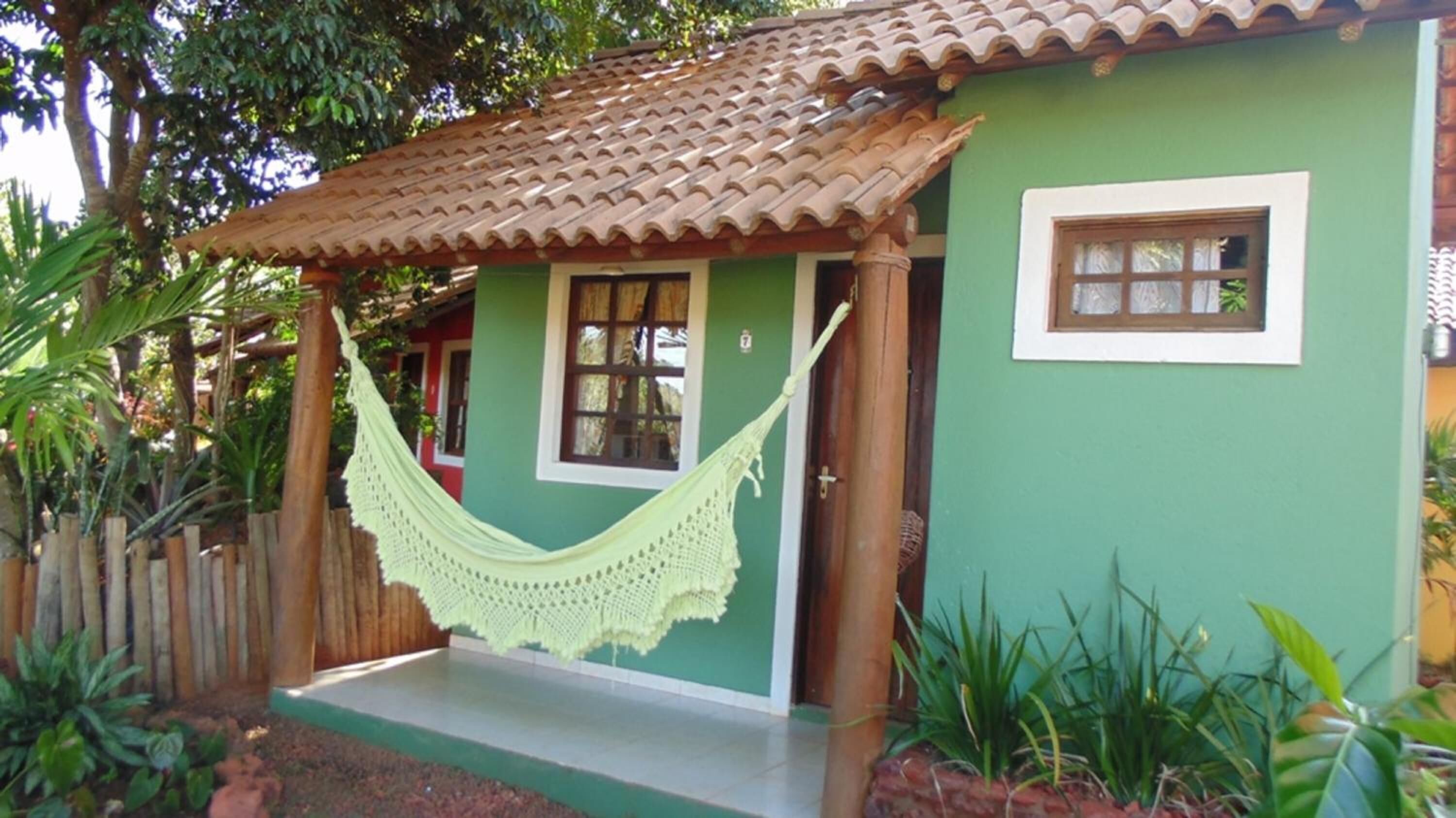 Uma casa verde com telhado de telhas, uma rede e uma cerca de madeira.