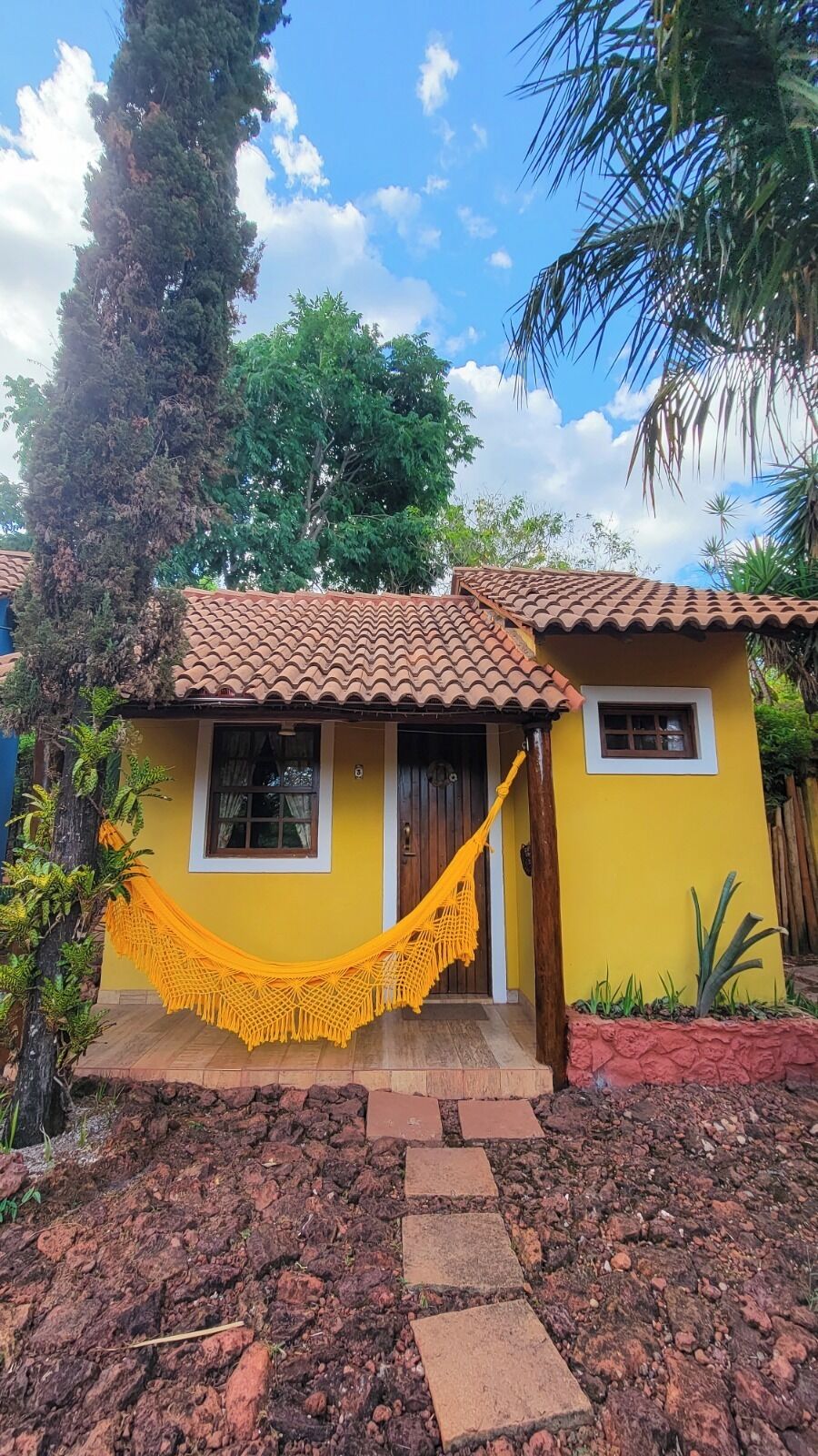 A yellow house with a tiled roof, a hammock, and a stone pathway leading to the entrance.