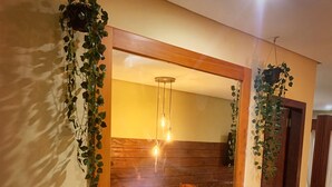 A room with a wooden-framed mirror reflecting a dining area, a wooden table, and chairs. There are hanging plants on either side of the mirror. - Pousada Oasis Paracuru (Paracuru)