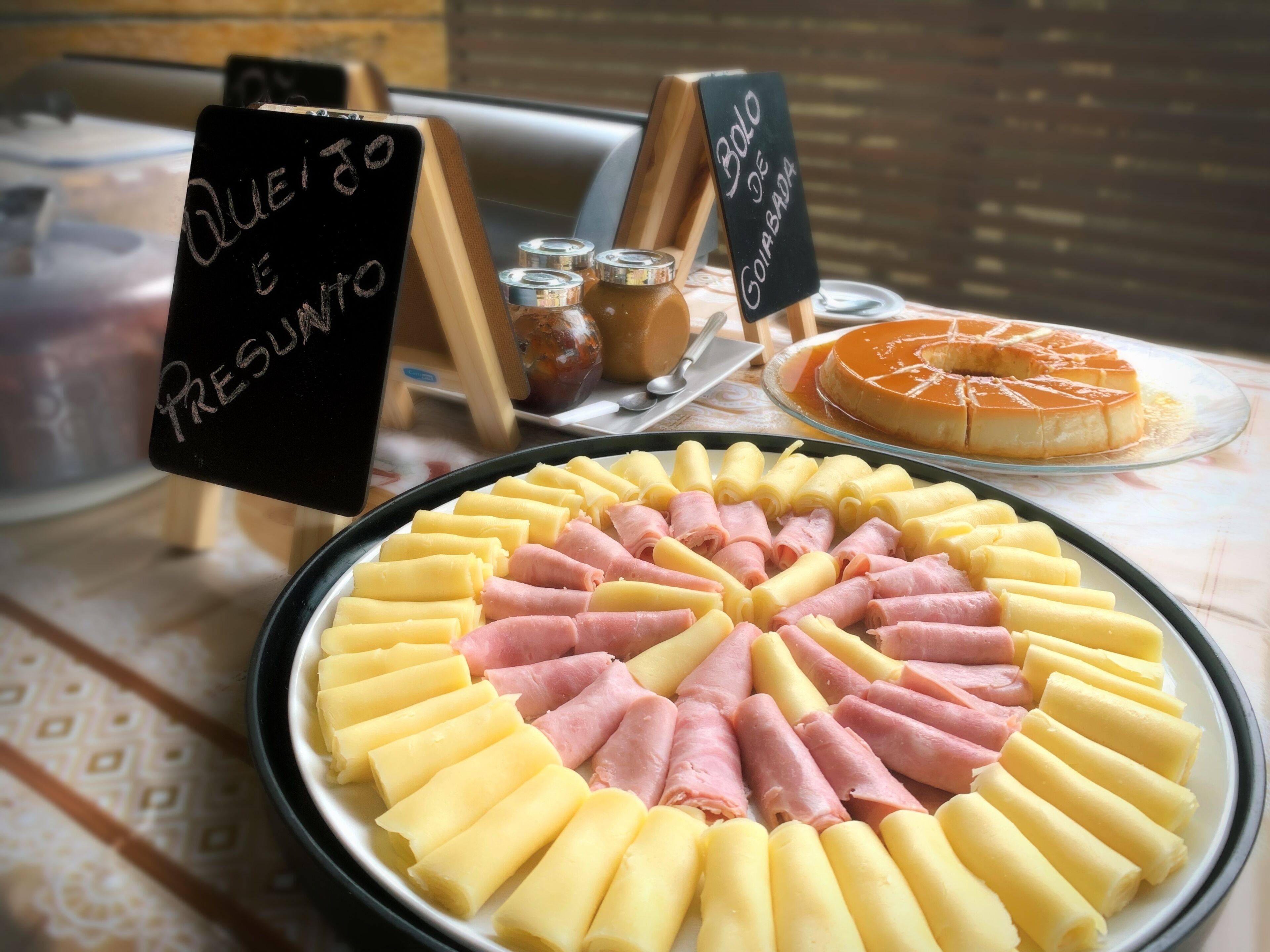 Una mesa con diversos alimentos, incluyendo un arreglo circular de panes amarillos y rosados, un flan de caramelo, y un letrero que anuncia una oferta especial.