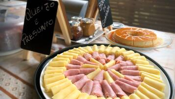 Una mesa con diversos alimentos, incluyendo un arreglo circular de panes amarillos y rosados, un flan de caramelo, y un letrero que anuncia una oferta especial.