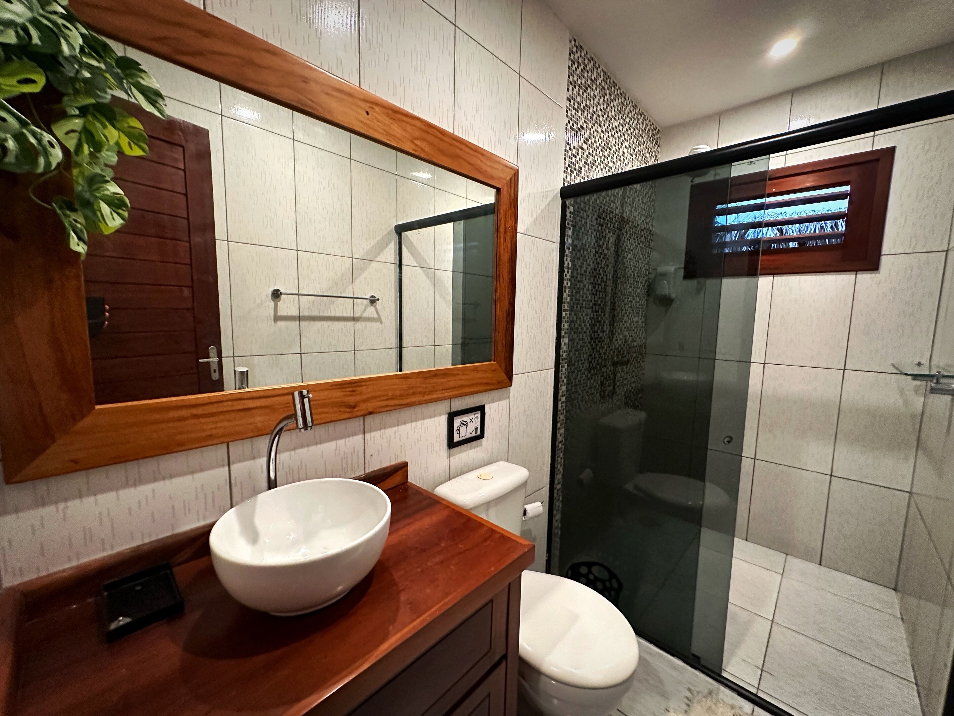 Ein Badezimmer mit einem Holzbadezimmer-Möbel, einem weißen Waschbecken, einem Spiegel, einer Toilette und einer Duschkabine.