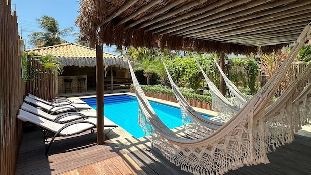 A pool area with a hammock, lounge chairs, and a thatched roof structure. - Pousada Oasis Paracuru (Paracuru)