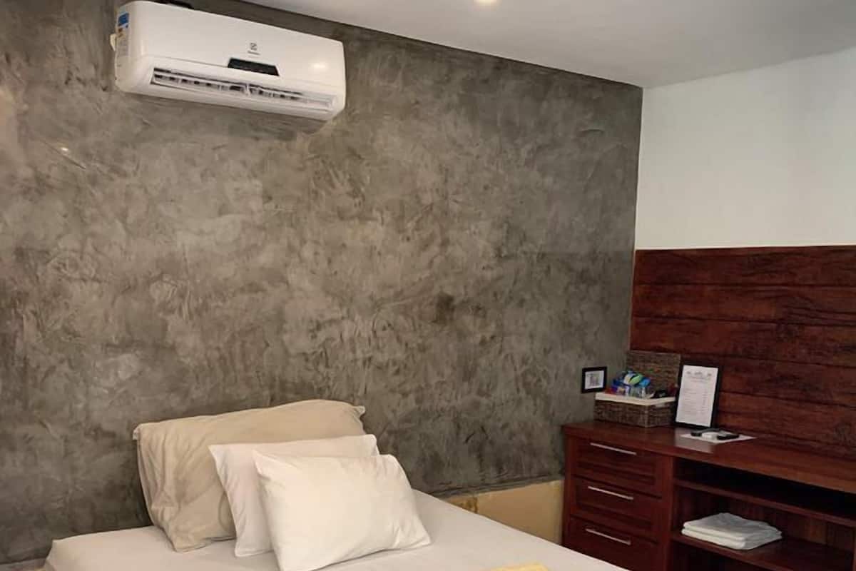 Un dormitorio con cama, mesita de noche de madera, escritorio y unidad de aire acondicionado en la pared.