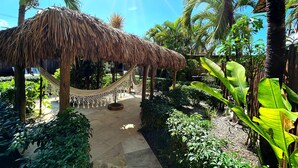 A thatched-roof structure with a hammock, surrounded by lush greenery and palm trees. - Pousada Oasis Paracuru (Paracuru)