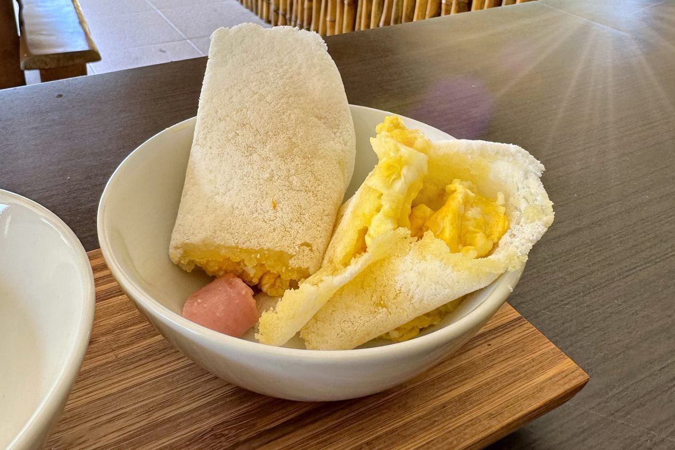 A bowl containing a rolled crepe with a sausage and scrambled eggs.