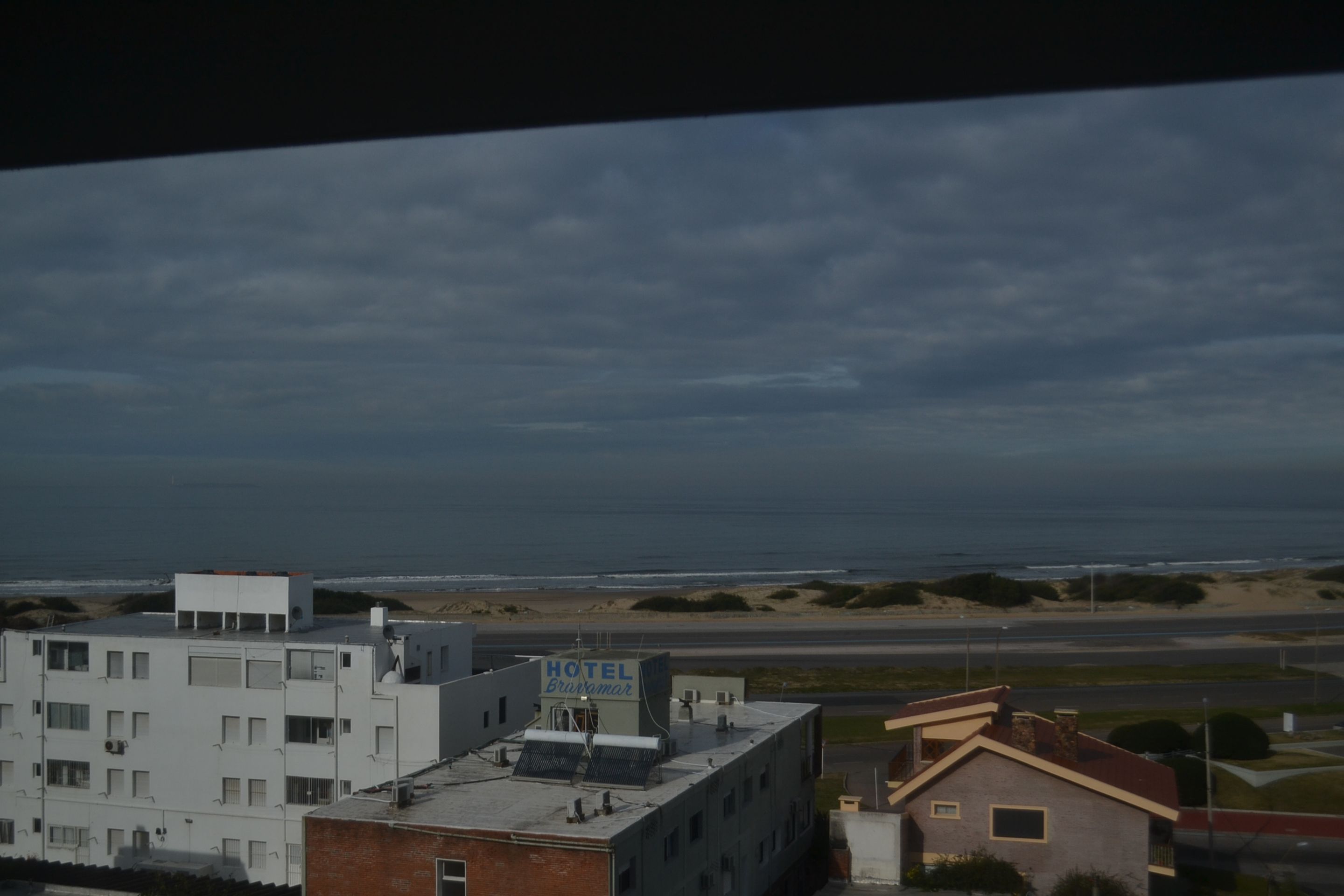 A hotel with a sign reading "HOTEL Granovam" on the rooftop, overlooking a beach and a road.