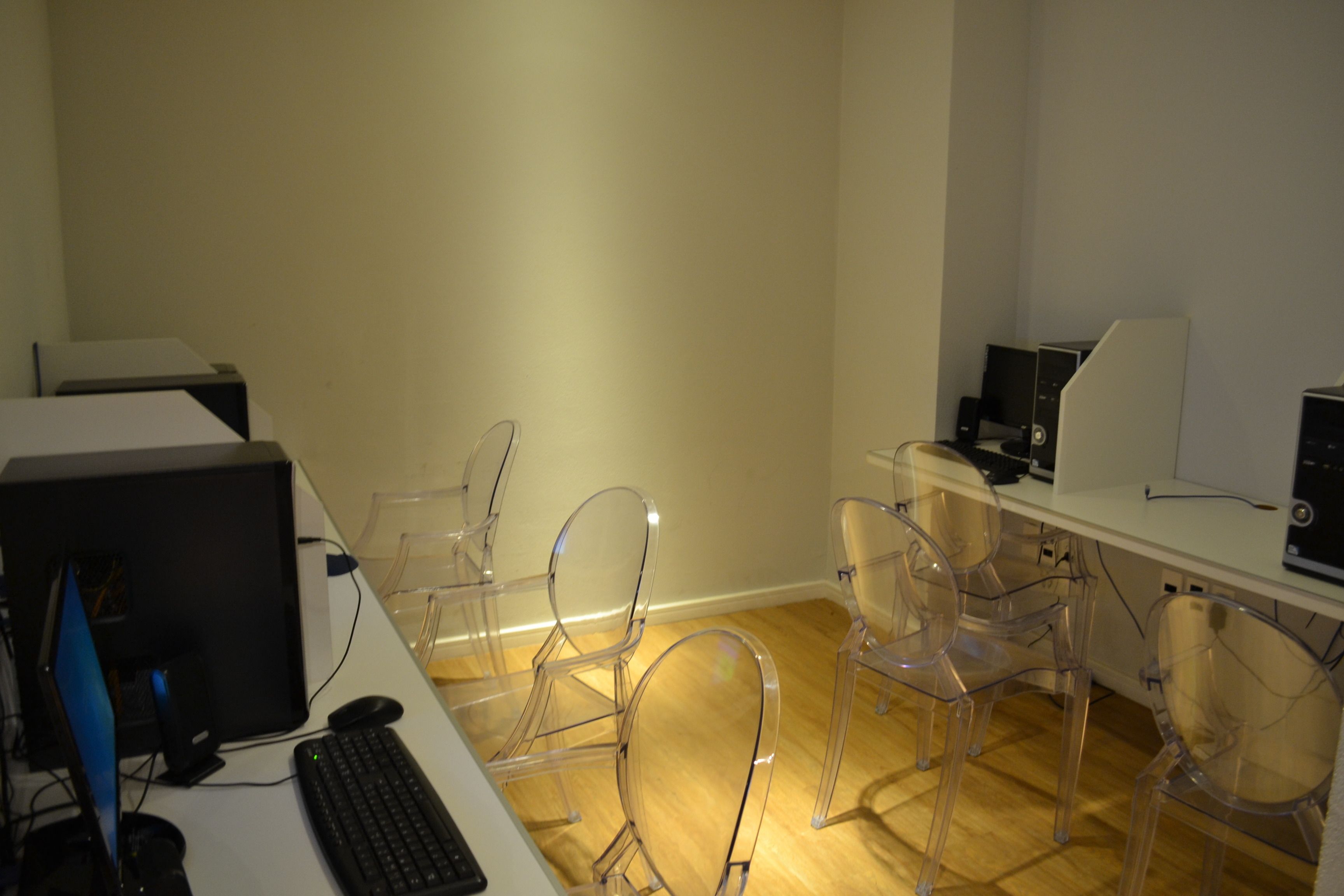 A room with a desk, computer, and clear plastic chairs.