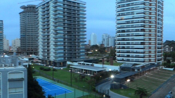 Zona urbana con edificios modernos, una cancha deportiva y una combinación de estructuras residenciales y comerciales.