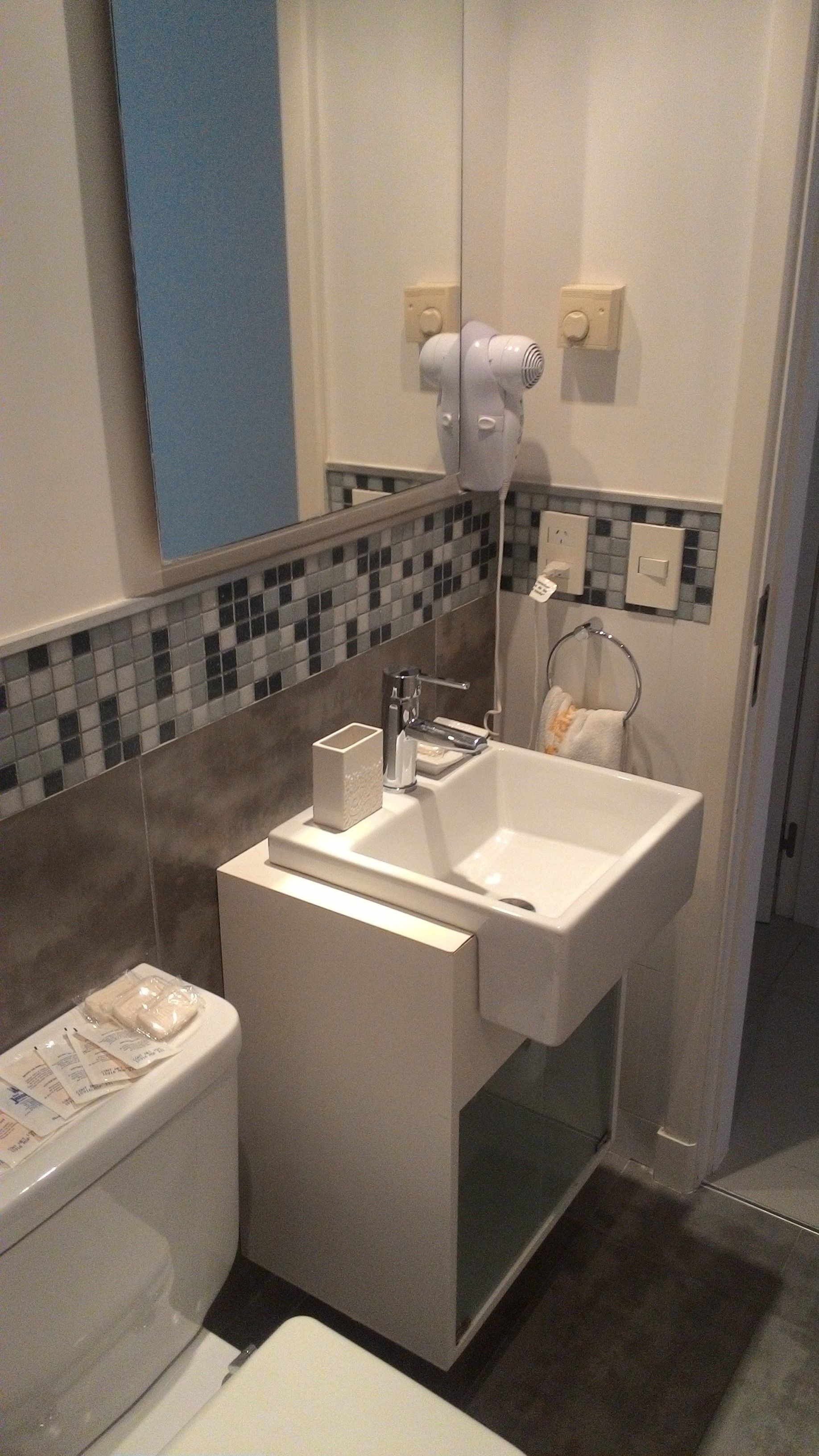 Un baño moderno con un lavamanos blanco, un espejo y un secador de pelo montado en la pared.