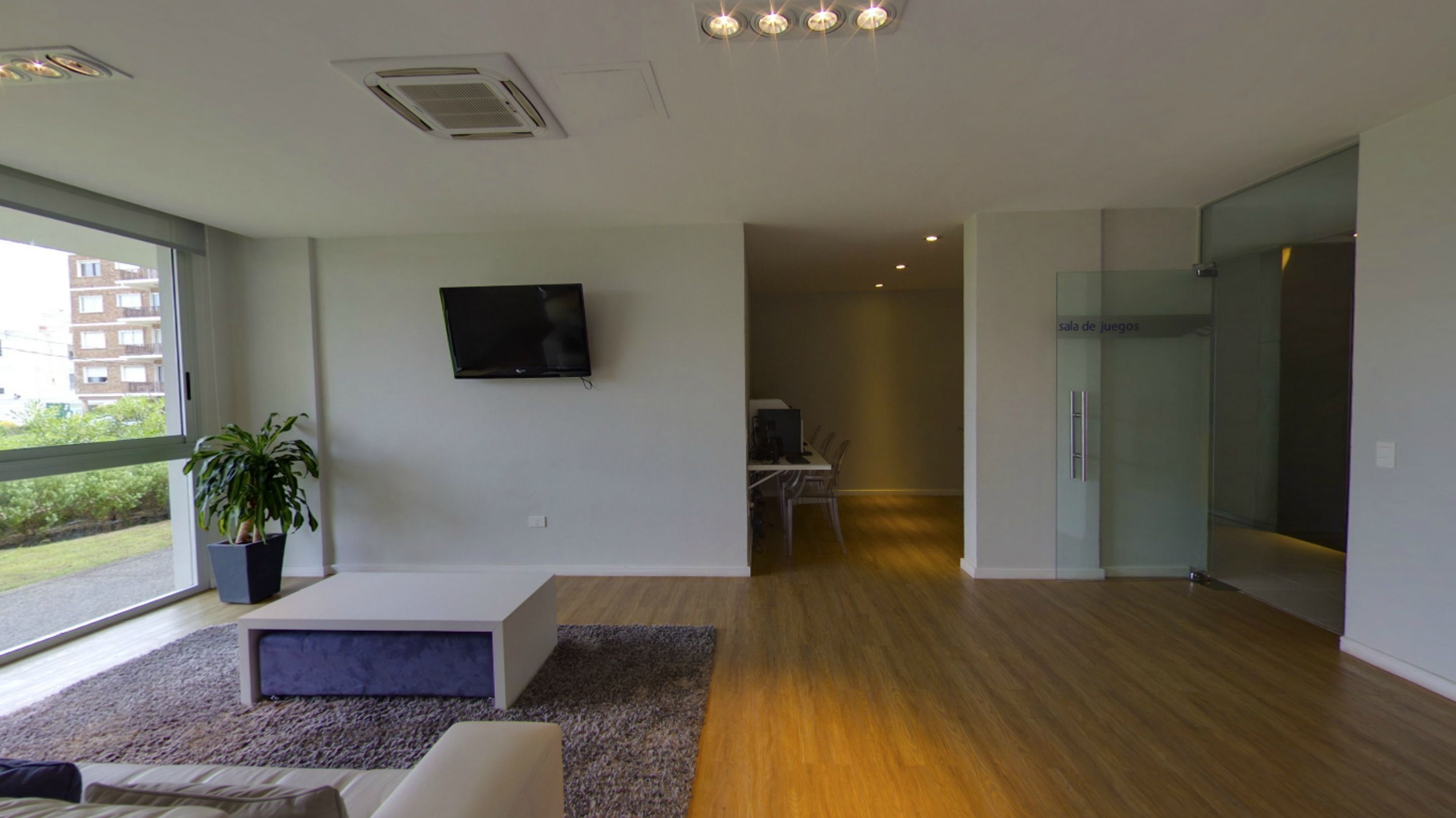 Una sala de estar moderna con un televisor de pantalla plana, una planta en maceta y un ventanal con vistas al exterior.