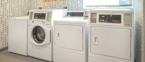 A laundry area with three front-loading washers and dryers, a window, and a wall with a motivational quote.