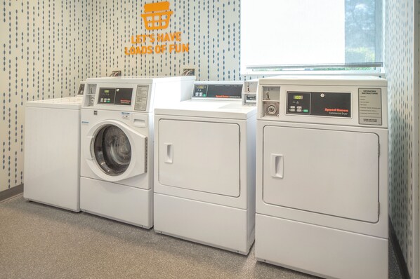 A laundry area with three front-loading washers and dryers, a window, and a wall with a motivational quote.