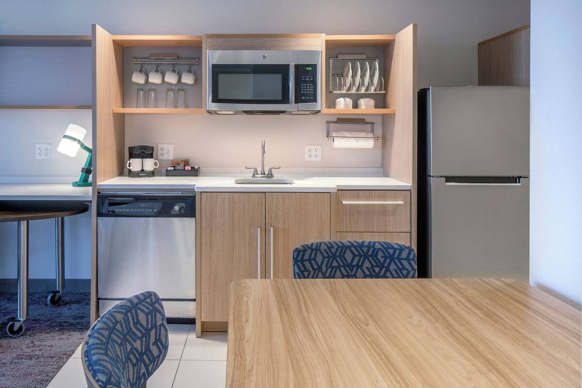 A compact kitchen with a microwave, coffee maker, and dishwasher. There is a dining table with chairs and a small rug.