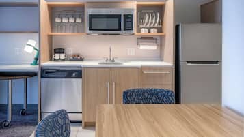 Uma cozinha compacta com micro-ondas, máquina de café e lava-louças. Há uma mesa de jantar com cadeiras e um tapete pequeno.
