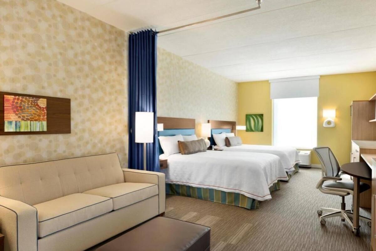 A hotel room with a sofa, two beds, a desk, and a chair.