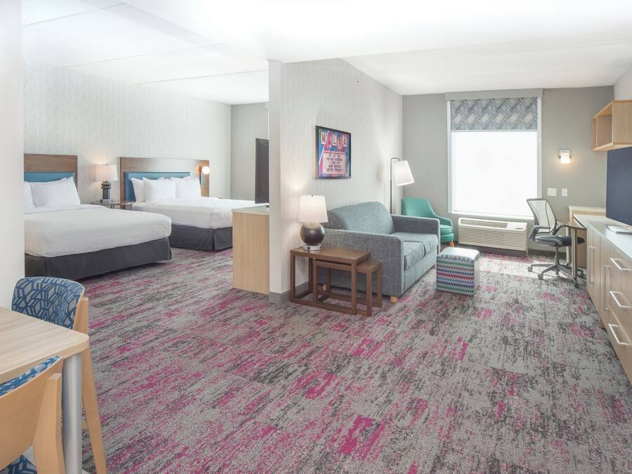 Een hotelkamer met twee bedden, een bureau, een stoel, een televisie en een raam met jaloezieën.