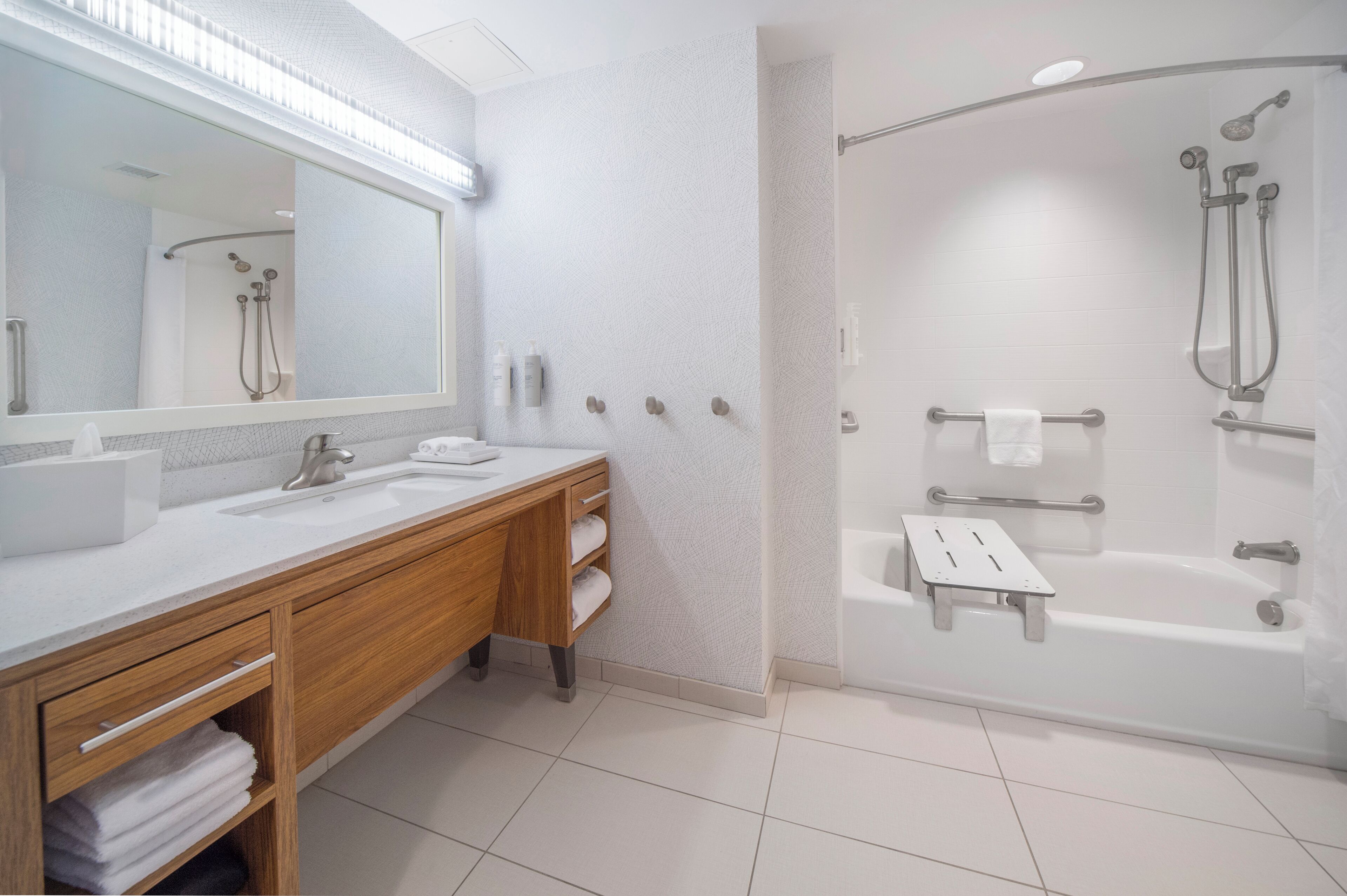 Un baño moderno con tocador de madera, un espejo grande, una bañera y zona de ducha.