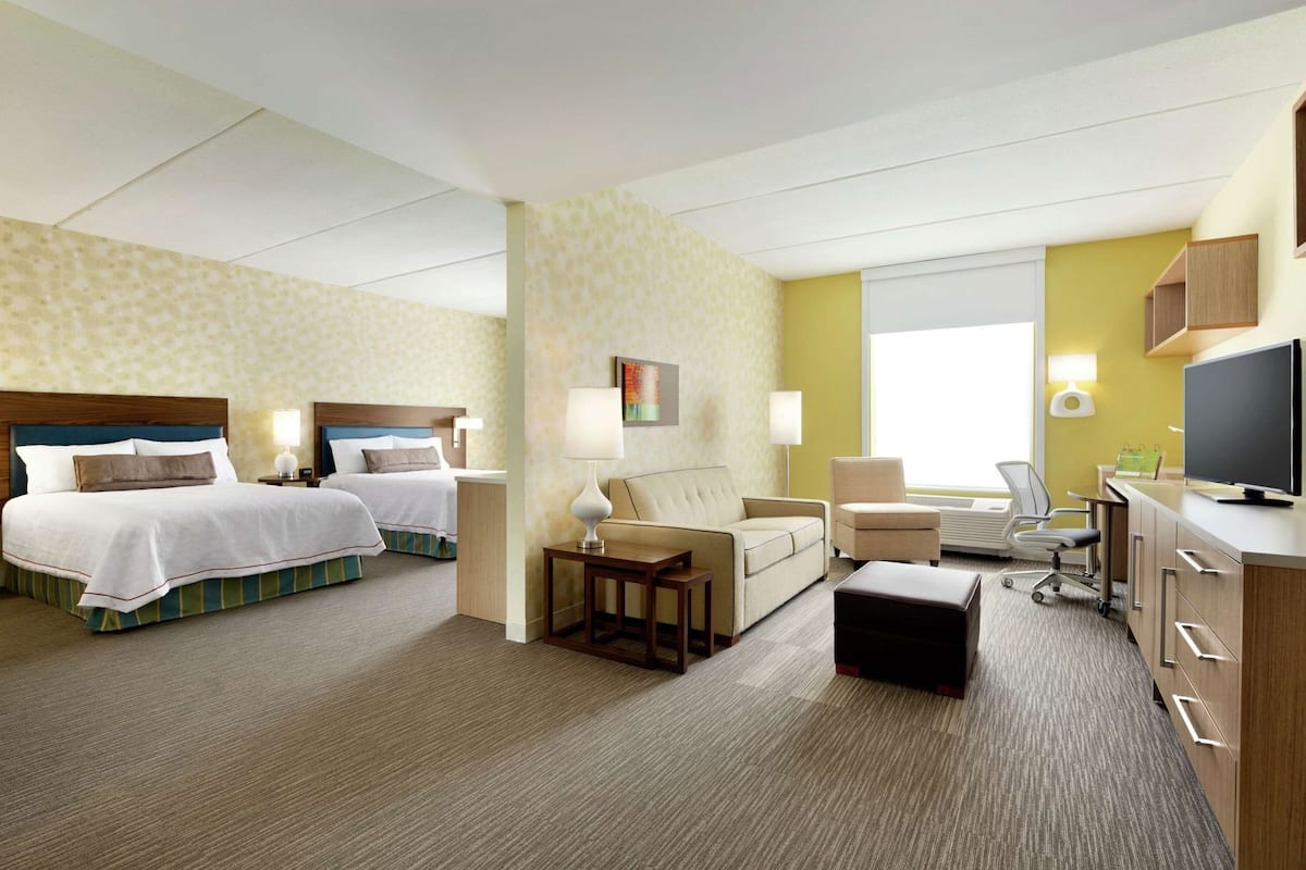 A hotel room with two beds, a sofa, a desk, a television, and a window.