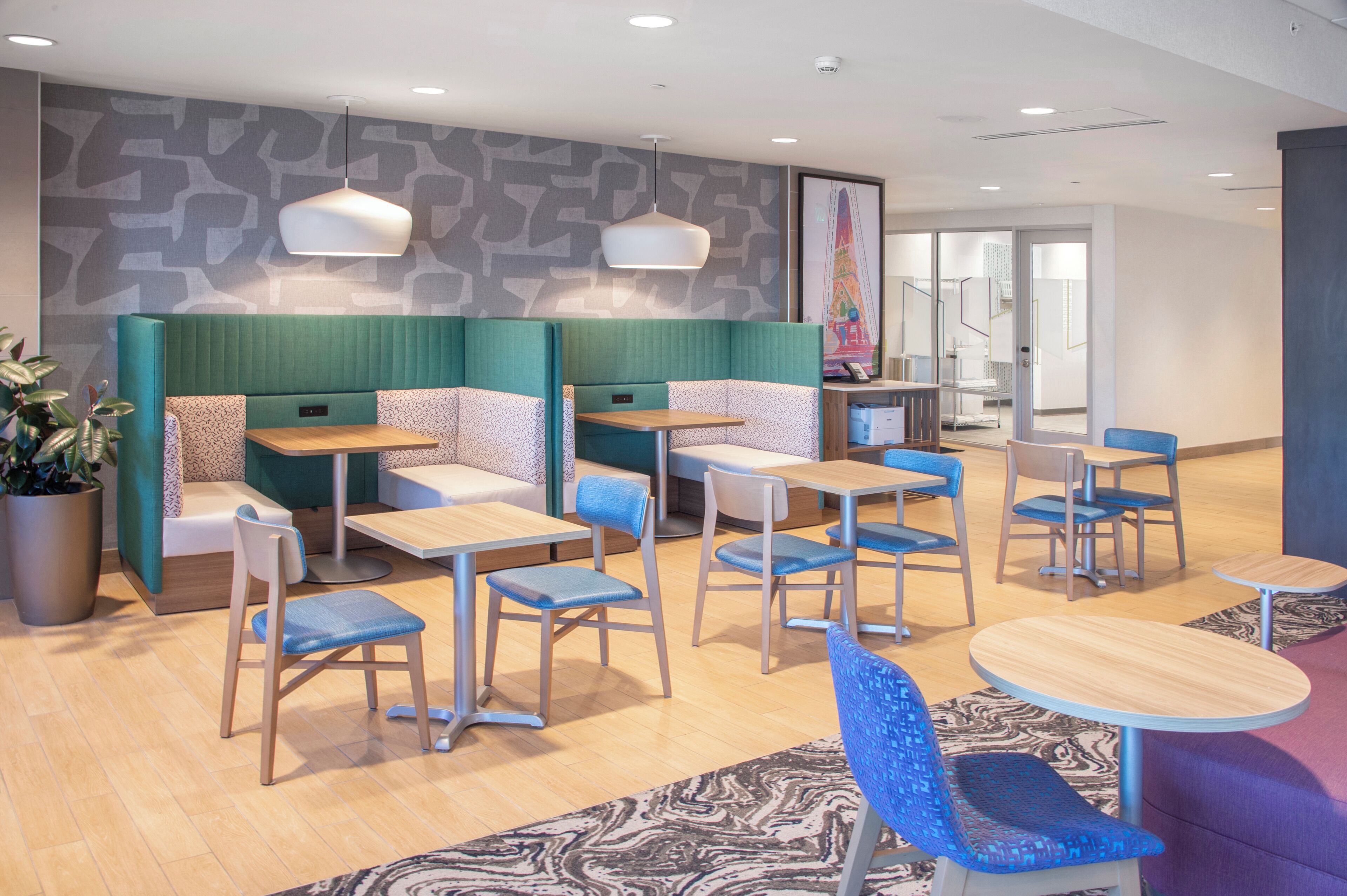 A modern dining area with booths and tables, featuring a patterned wall and a large potted plant.